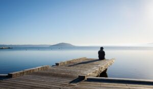 Person sitting quietly beside the water with space for reflection and stillness.